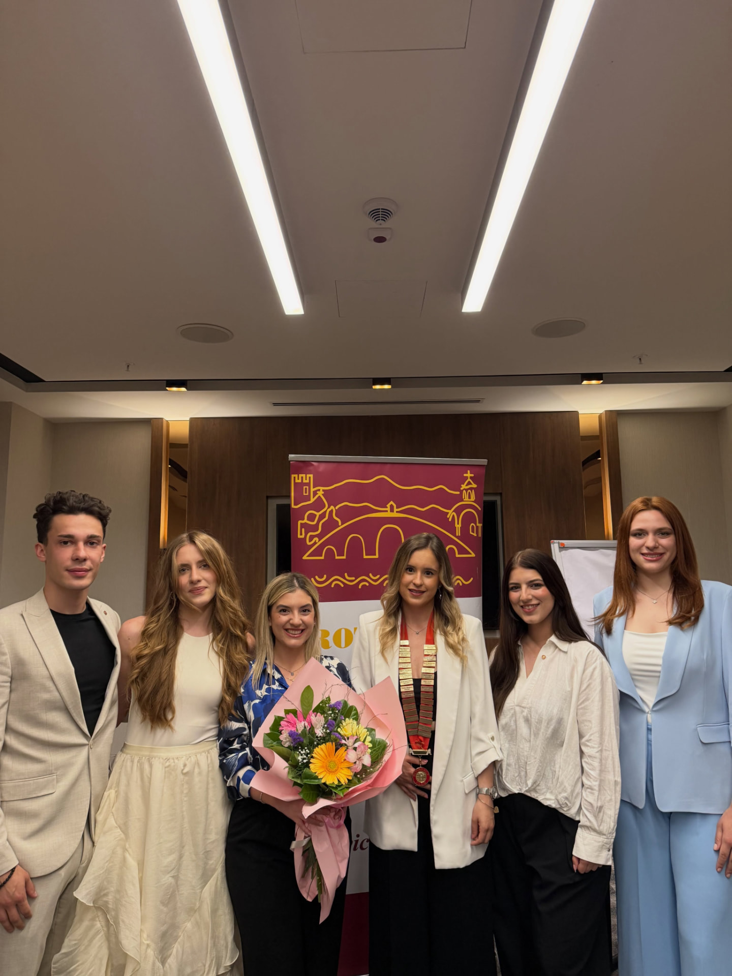 A smaller group of members gathered beside the club banner, one holding a bouquet of flowers during a club occasion.